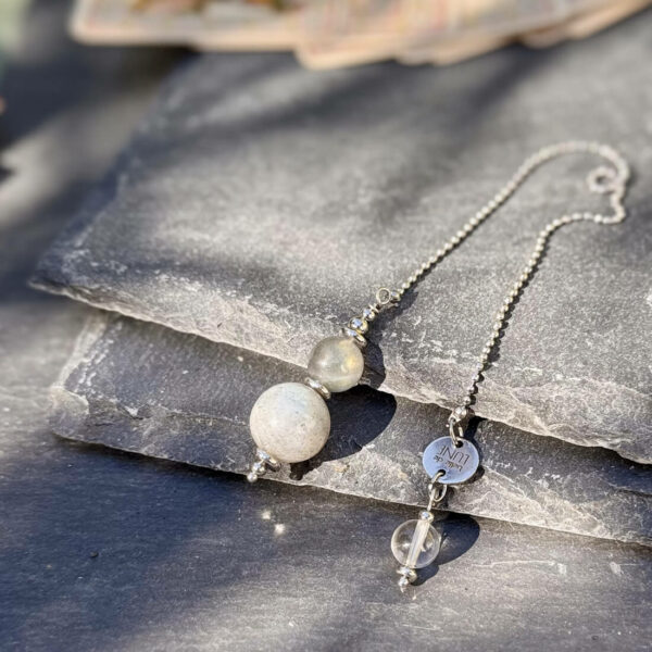 Pendule en labradorite tenu dans une main de femme, outil de divination et d’intuition.
