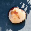 coeur-cornaline-profil-blanc-creme-inclusions-soleil Vue de profil d'un coeur en cornaline naturelle aux tons blanc crème et orangé, posé sur fond bleu en pleine lumière. Les inclusions minérales caractéristiques de la cornaline de Madagascar sont visibles en détail. Idée cadeau lithothérapie pour femme.