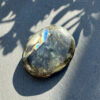 galet-labradorite-main-reflets-jaune-vert-bleu-jardin Galet en labradorite naturelle de Madagascar tenu dans une main en extérieur, avec une labradorescence jaune-vert et bleue exceptionnelle visible sur la surface polie. Pierre lithothérapie pour les personnes sensibles et empathiques. Cadeau bien-être femme. Belle de Lune Bijoux.